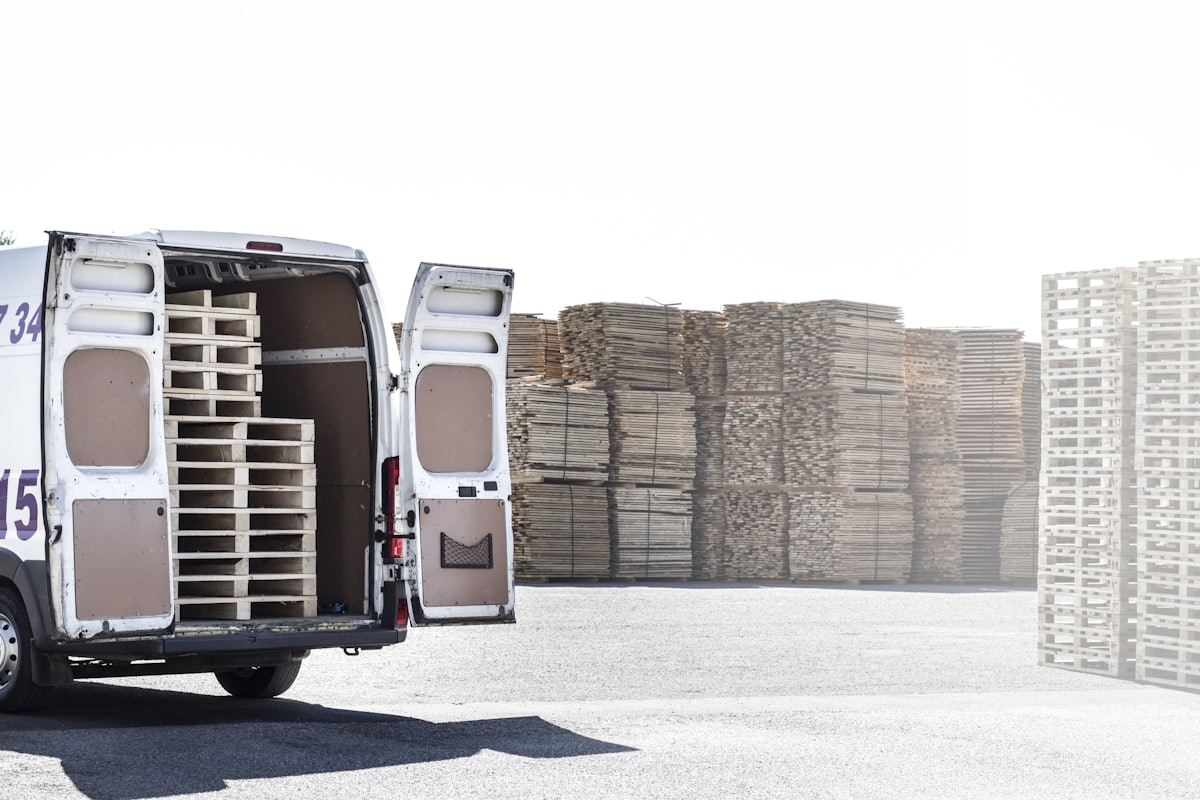 Furgoneta con palés de madera cargados junto a una pila de palés